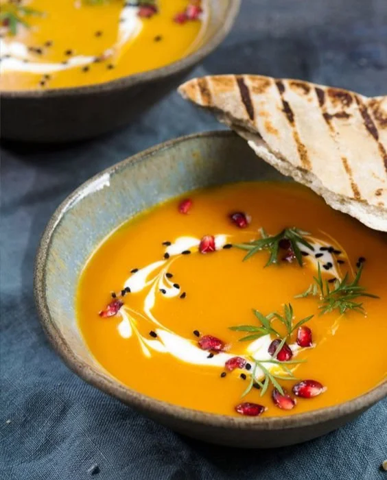 Eine Schüssel Kürbiscremesuppe mit Kürbisstücken und frischen Kräutern