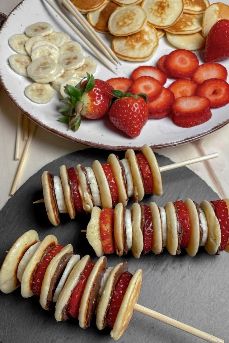 Mini Pancake Spieße mit Erdbeeren, Banane und Schokocreme auf einem Tisch serviert