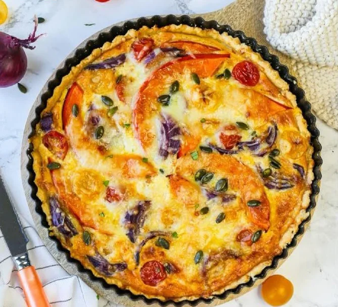 Saftige Kürbis-Quiche mit Feta auf einem Teller, garniert mit frischen Kräutern