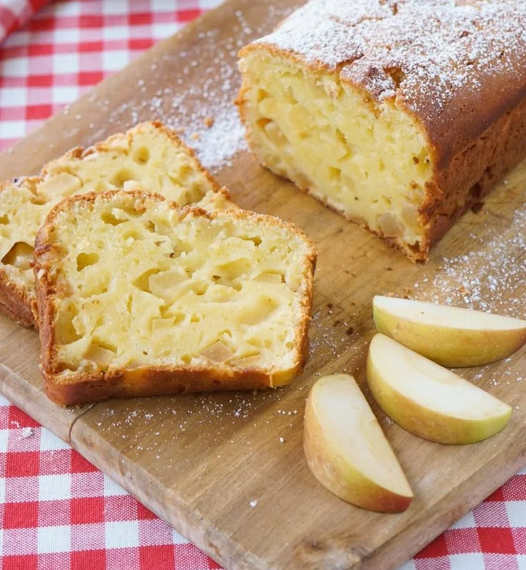 Ein Stück saftiger Apfelkuchen mit frischen Äpfeln auf einem Teller.